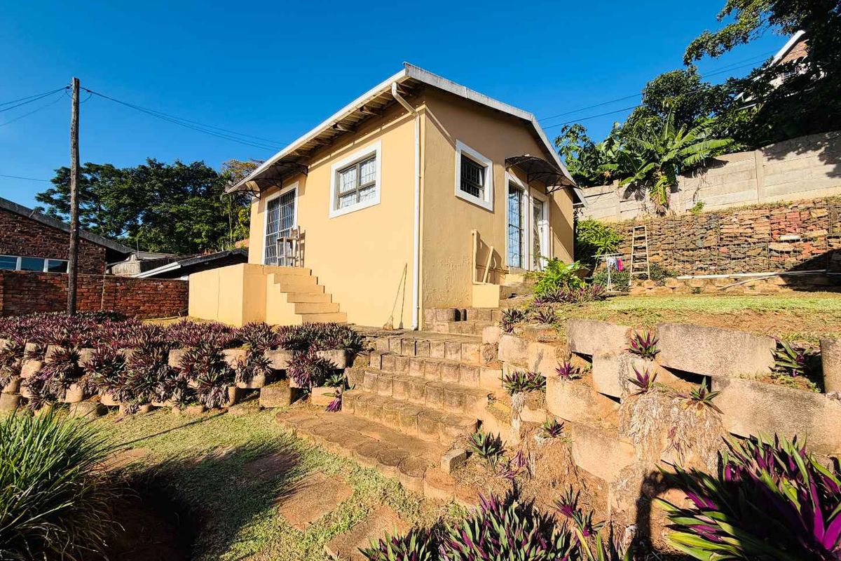 A rear view of a detached house featuring a terraced garden with stone retaining walls and concrete steps leading to the building entrance.