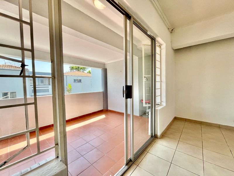 A spacious, empty balcony featuring tiled flooring, secure sliding glass doors, and a protective railing, offering a clean outdoor space for relaxation.