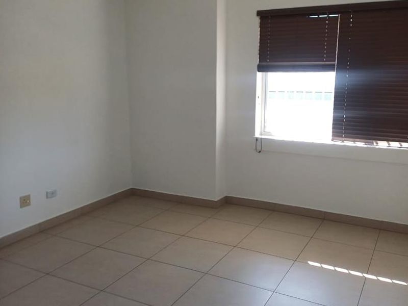 A clean, empty office space featuring tiled flooring, a suspended ceiling with recessed lighting, and a wall-mounted air conditioning unit.