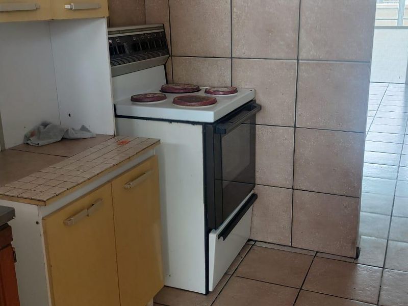 A functional kitchen featuring tiled flooring, a tiled splashback, built-in cabinetry, and a freestanding stove, offering potential for modernization and cosmetic updates.