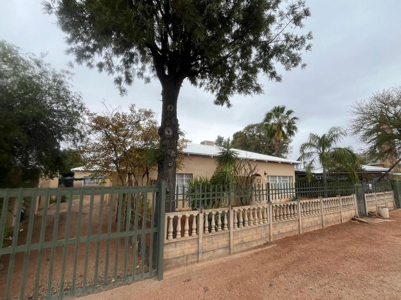 Front view of a single-story house featuring a metal perimeter fence, concrete balustrade wall, and a corrugated metal roof.