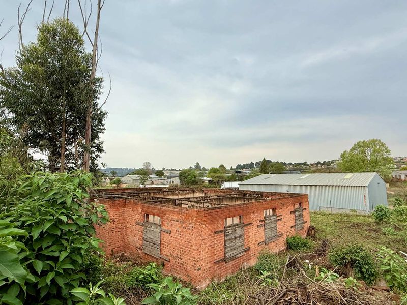 A view of a derelict brick structure on a vacant commercial plot, featuring exposed masonry walls and boarded-up window openings.