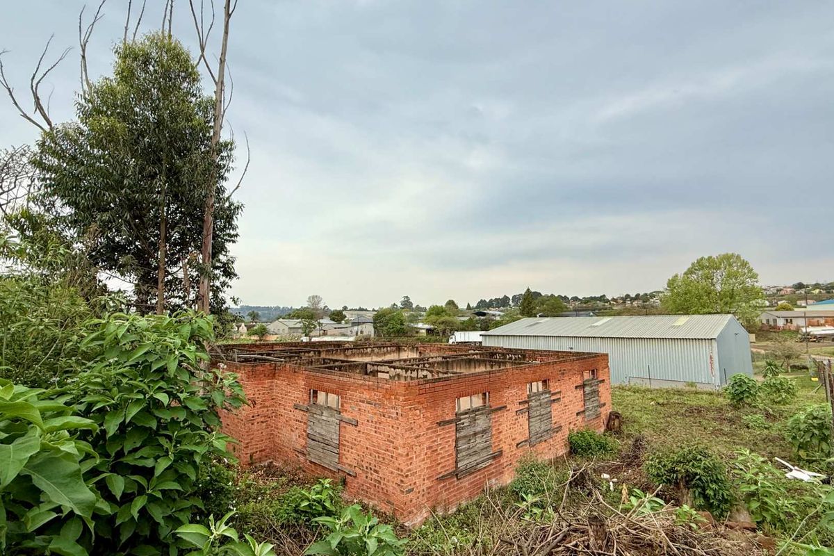 A view of a derelict brick structure on a vacant commercial plot, featuring exposed masonry walls and boarded-up window openings.