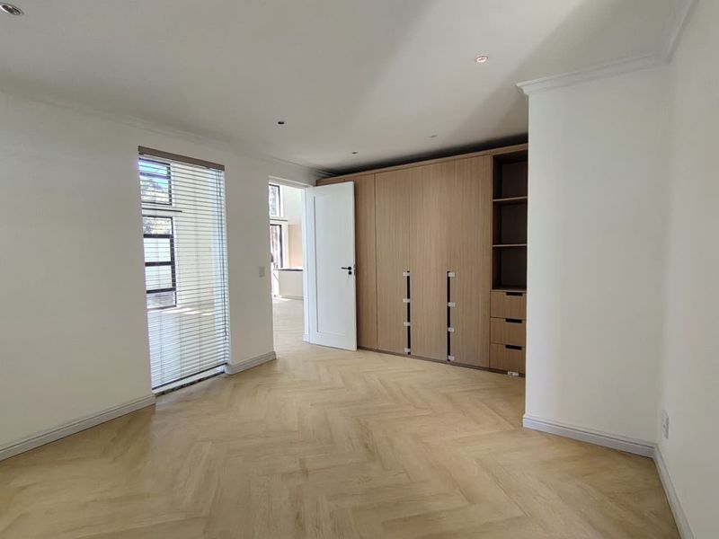 A bright, modern bedroom featuring light herringbone flooring, built-in wooden cabinetry, and recessed lighting, offering a clean and neutral space.
