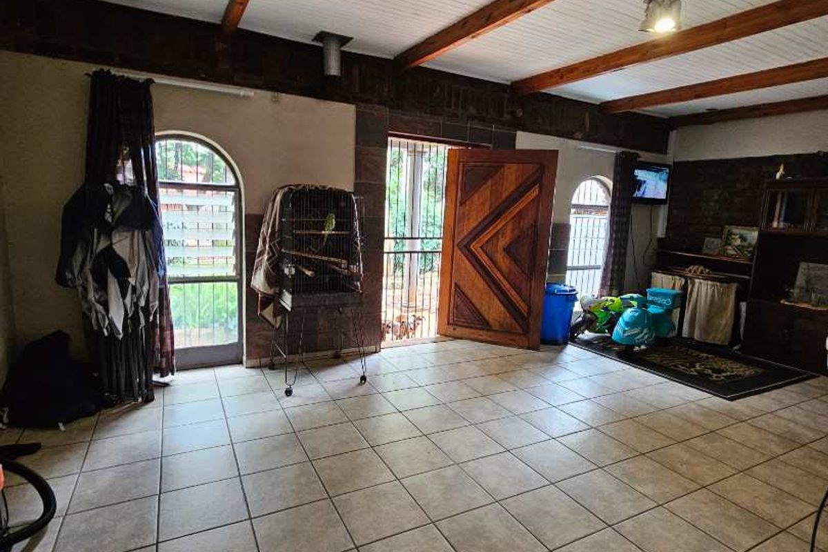 Spacious living area featuring tiled flooring, exposed timber ceiling beams, and arched doorways leading to the exterior.