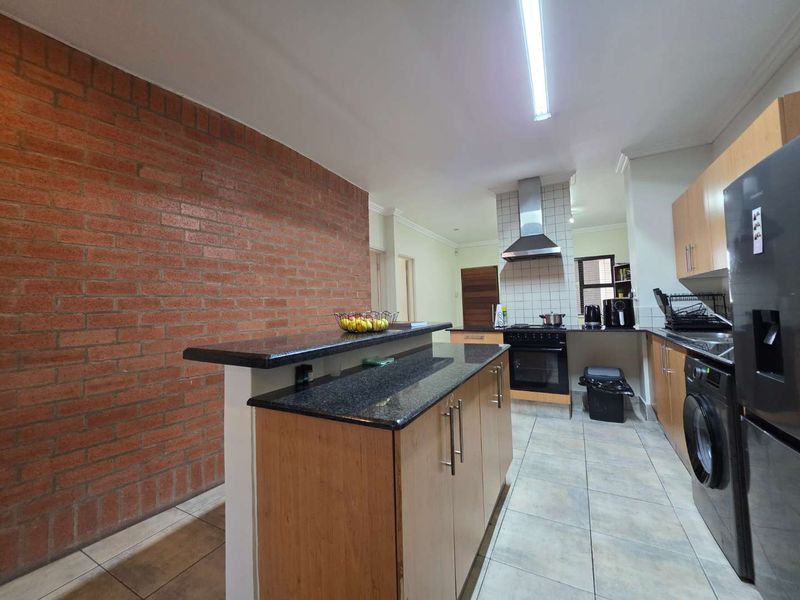 A functional kitchen featuring wooden cabinetry, granite countertops, a breakfast bar, and a distinctive exposed brick feature wall with tiled flooring.