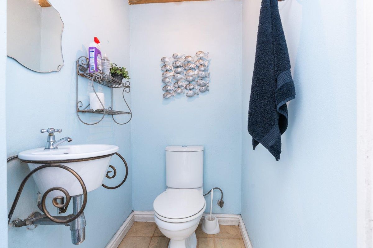 A compact guest bathroom featuring a wall-mounted basin with decorative metal supports and a standard white toilet.