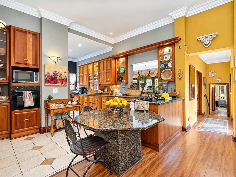 Spacious kitchen featuring timber cabinetry, granite countertops, built-in appliances, and a central island, seamlessly transitioning into the living area with elegant crown molding.