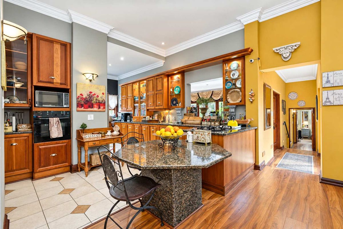 Spacious kitchen featuring timber cabinetry, granite countertops, built-in appliances, and a central island, seamlessly transitioning into the living area with elegant crown molding.