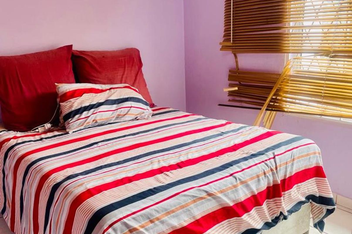 A bedroom featuring tiled flooring and venetian blinds, showing signs of wear including cracked wall plaster and damaged window coverings.