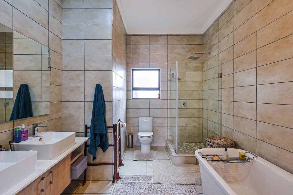Modern bathroom featuring a double vanity, glass-enclosed rain shower, and a freestanding bathtub with neutral floor-to-ceiling ceramic tiling.