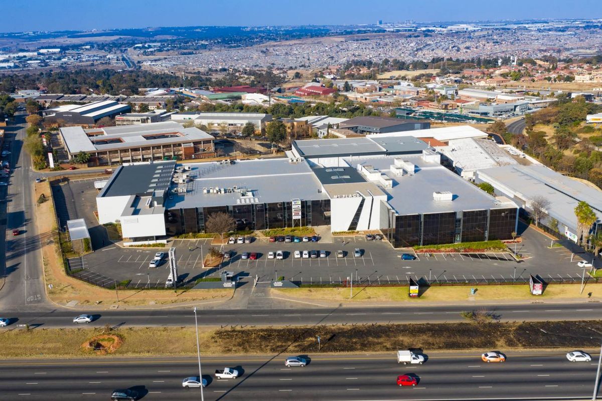 Aerial view of a large industrial commercial property featuring extensive parking facilities, modern building facade, and metal roofing, situated near a major roadway.