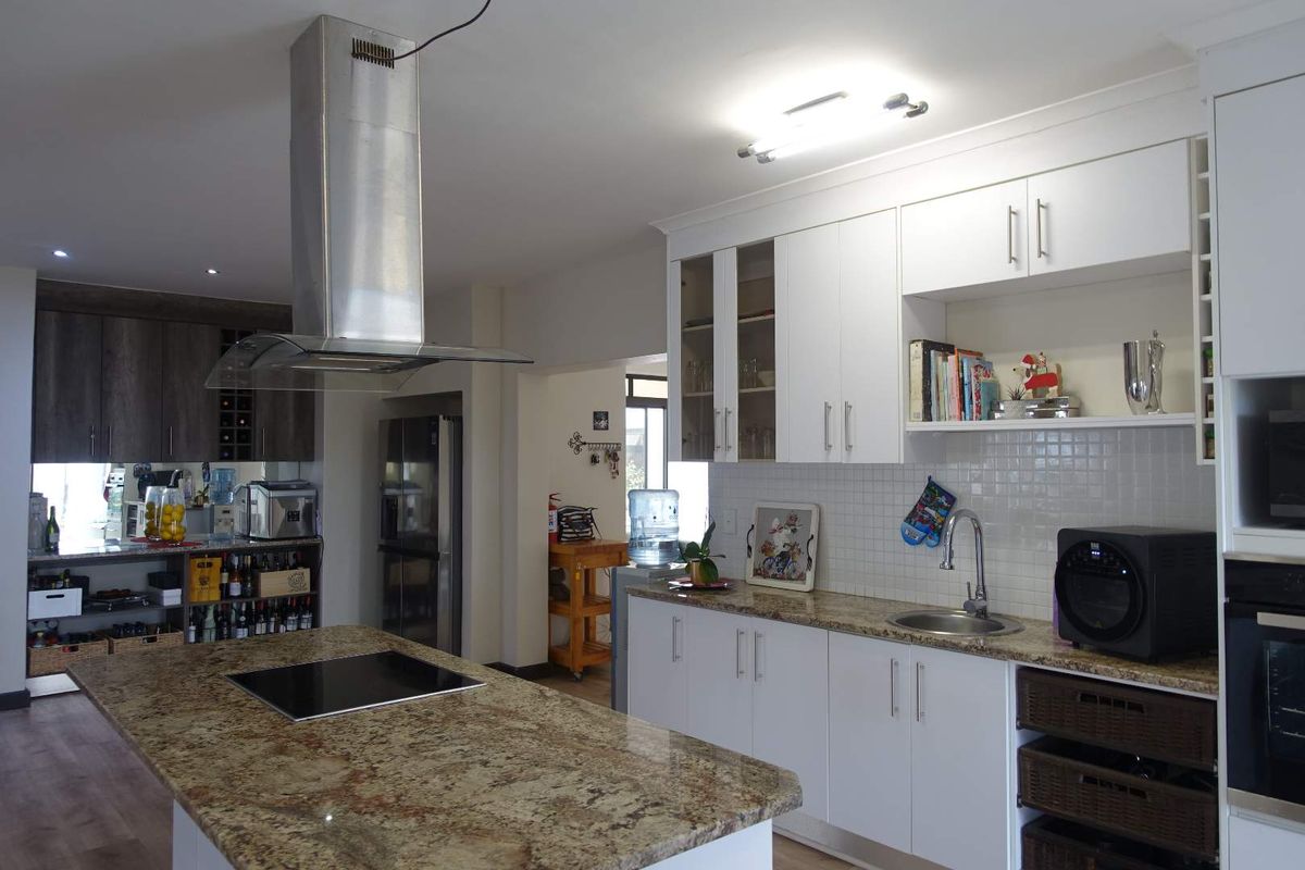 Modern kitchen featuring a central island with a built-in hob, stainless steel extractor fan, granite countertops, and white cabinetry.