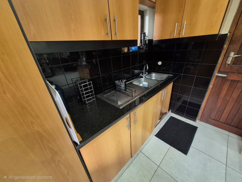 Compact kitchen featuring wood-look laminate cabinetry, black granite countertops, a double stainless steel sink, and black tiled splashbacks.