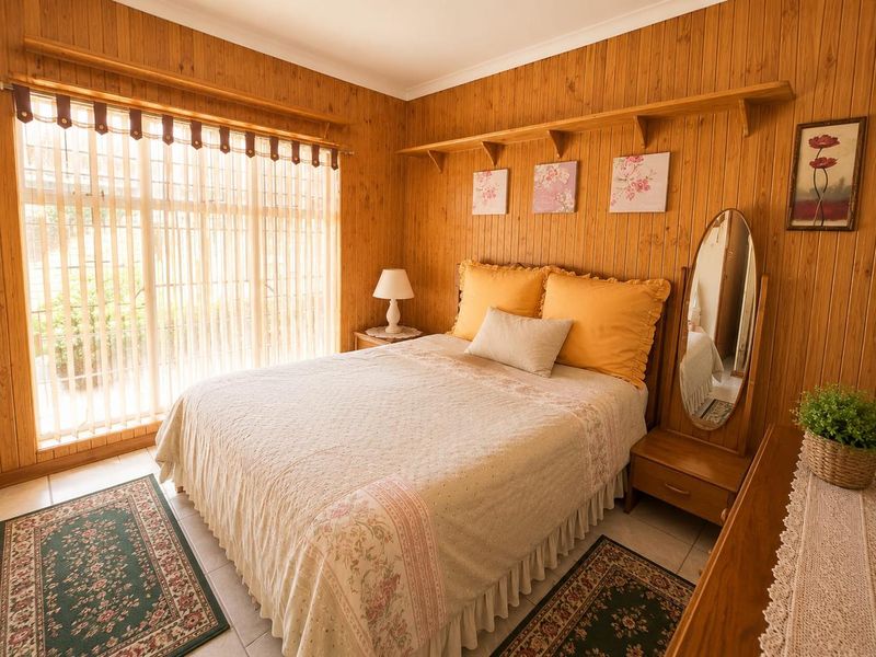 A cozy bedroom featuring warm timber wall paneling, tiled flooring, and large windows with vertical blinds, offering a classic and comfortable living space.