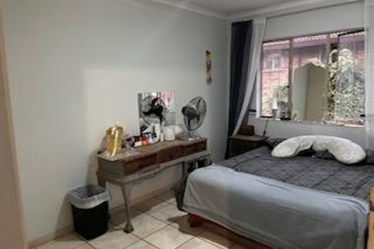 A functional bedroom featuring tiled flooring and a large window providing natural light, suitable for comfortable living.