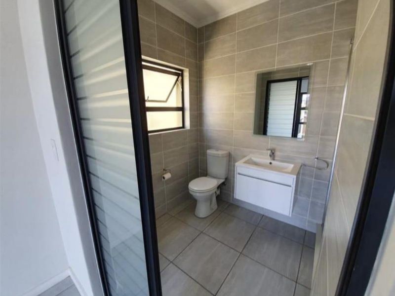 A modern, well-maintained bathroom featuring neutral floor-to-ceiling tiling, a wall-mounted vanity with basin, and a functional casement window.