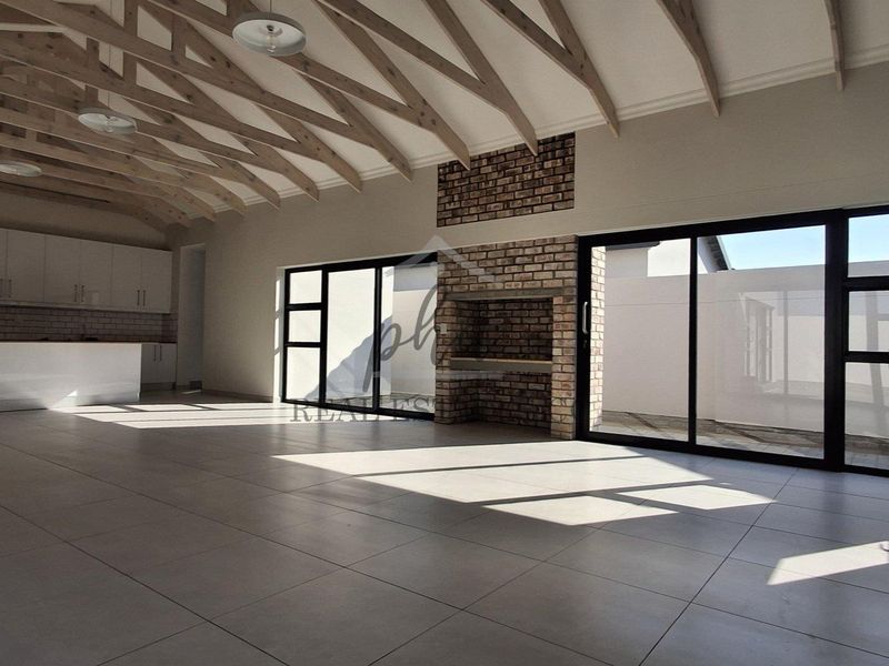 Spacious open-plan living area featuring exposed timber trusses, a built-in brick fireplace, modern kitchen cabinetry, and large sliding doors leading to the exterior.