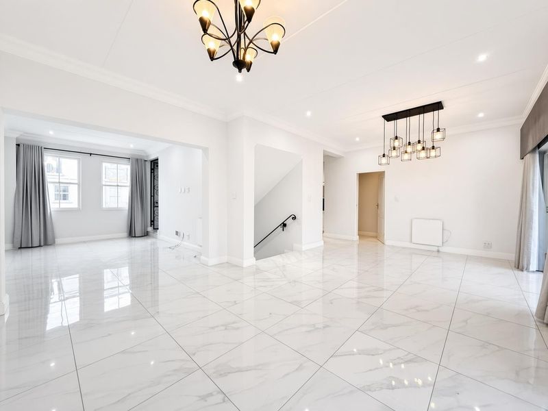 Spacious open-plan living area featuring polished marble-look floor tiles, modern lighting fixtures, and a staircase with a decorative wrought iron railing.