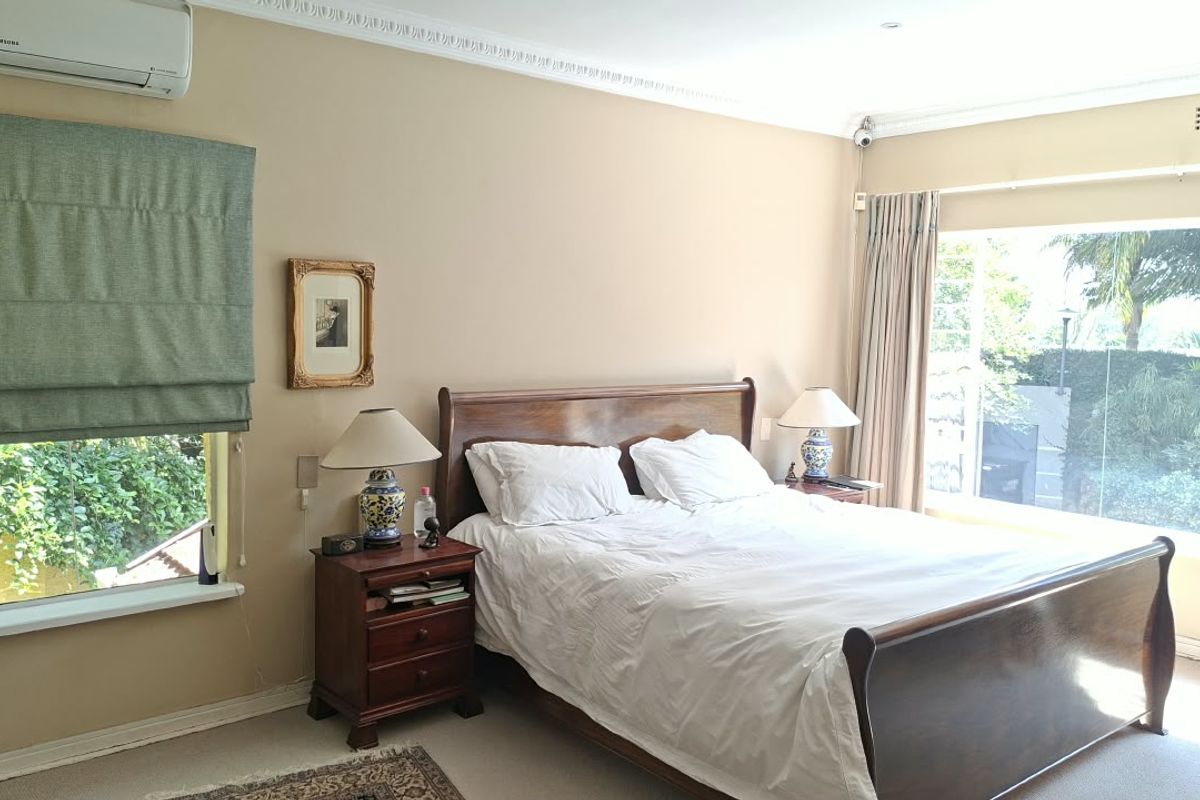 A well-lit bedroom featuring decorative ceiling cornicing, a split-system air conditioner, and a large window overlooking the garden.