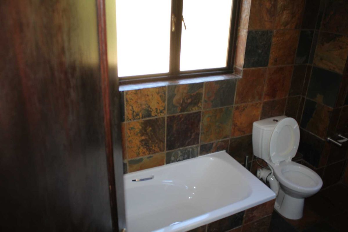 A functional bathroom featuring a built-in bathtub, a standard toilet, and distinctive slate wall tiling under a window.