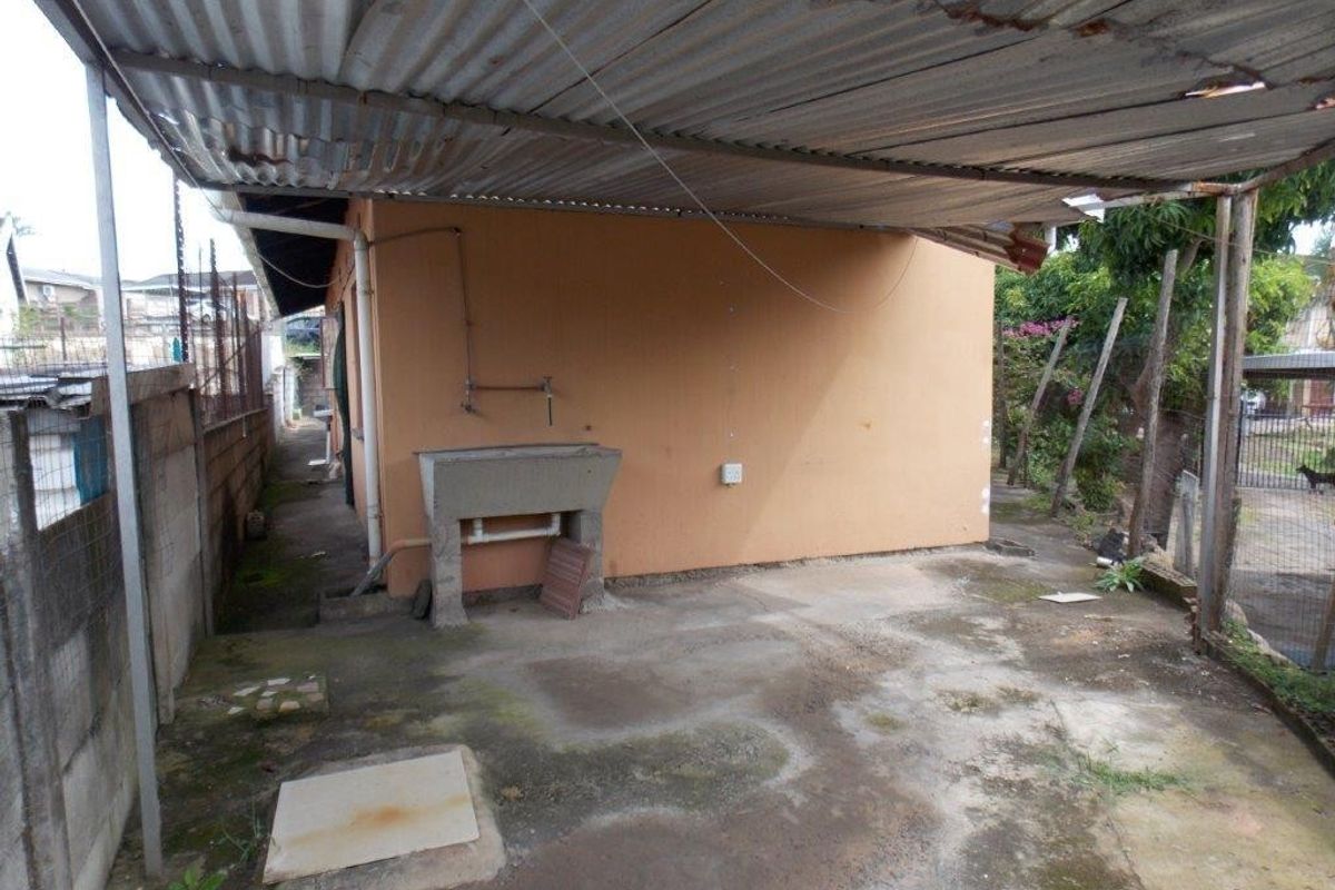 Rear exterior area featuring a covered concrete patio with a utility sink, corrugated metal roofing, and concrete slab flooring.