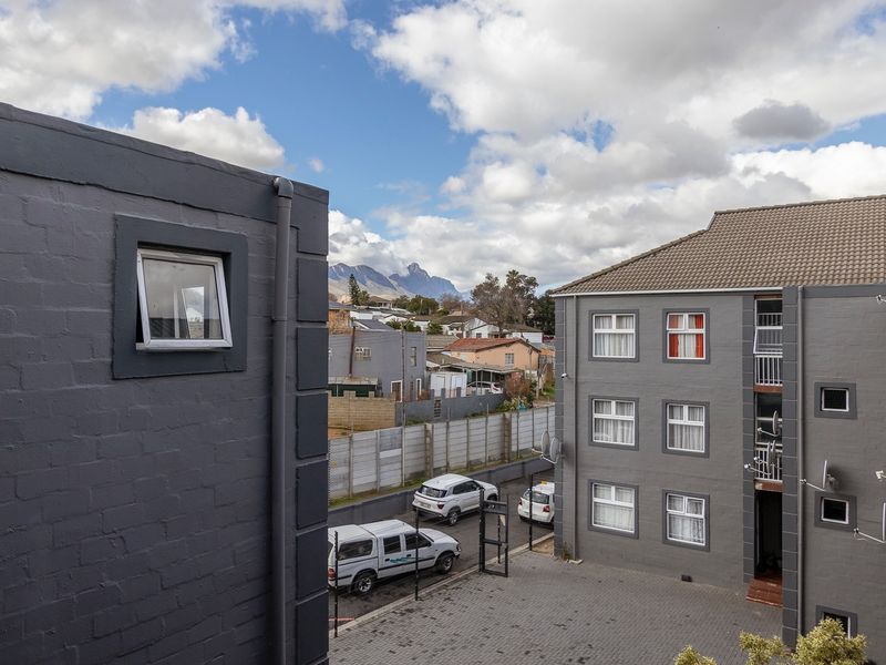 An elevated view of the apartment complex courtyard, featuring paved surfaces, painted brick exteriors, and a scenic mountain backdrop.