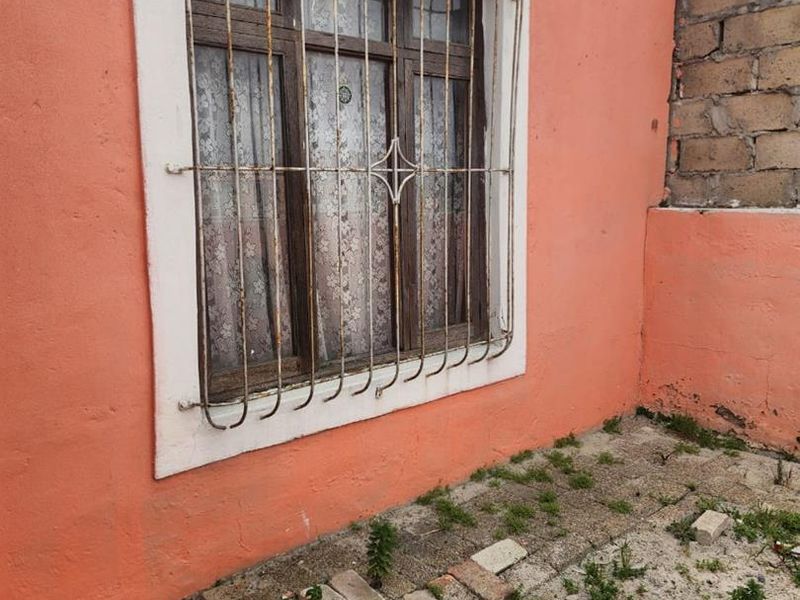 Exterior view of a residential wall featuring a timber window with a security gate, showing signs of wear and weathering.