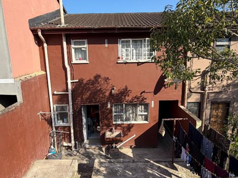 Rear exterior view of the townhouse featuring a concrete patio area, external wash basin, and metal staircase access.