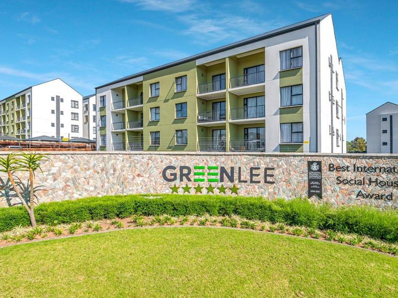 A well-maintained multi-story apartment complex featuring modern architecture, private balconies, and a landscaped front garden with stone feature wall.