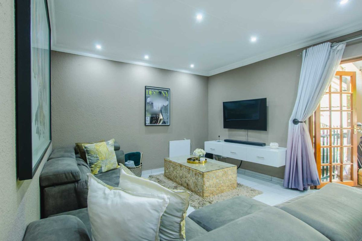A comfortable living room featuring recessed ceiling lighting, tiled flooring, and a wall-mounted television unit with direct access to an outdoor area.