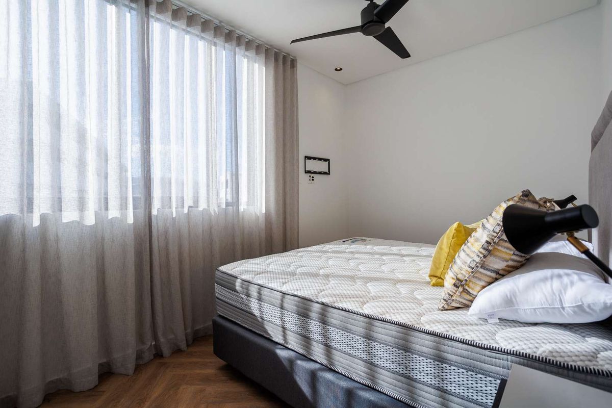 A modern, well-lit bedroom featuring elegant herringbone timber flooring, a sleek ceiling fan, and floor-to-ceiling sheer curtains.
