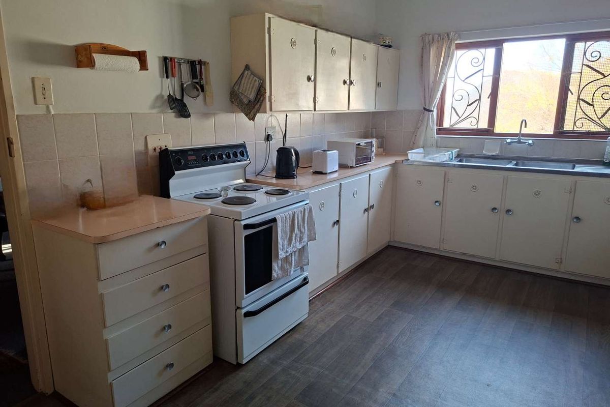 A functional kitchen featuring original cabinetry, laminate countertops, a freestanding stove, and a double-basin sink with security-grilled windows.