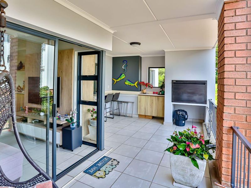 Covered balcony featuring tiled flooring, a built-in braai, and sliding glass doors providing seamless access to the interior living area.