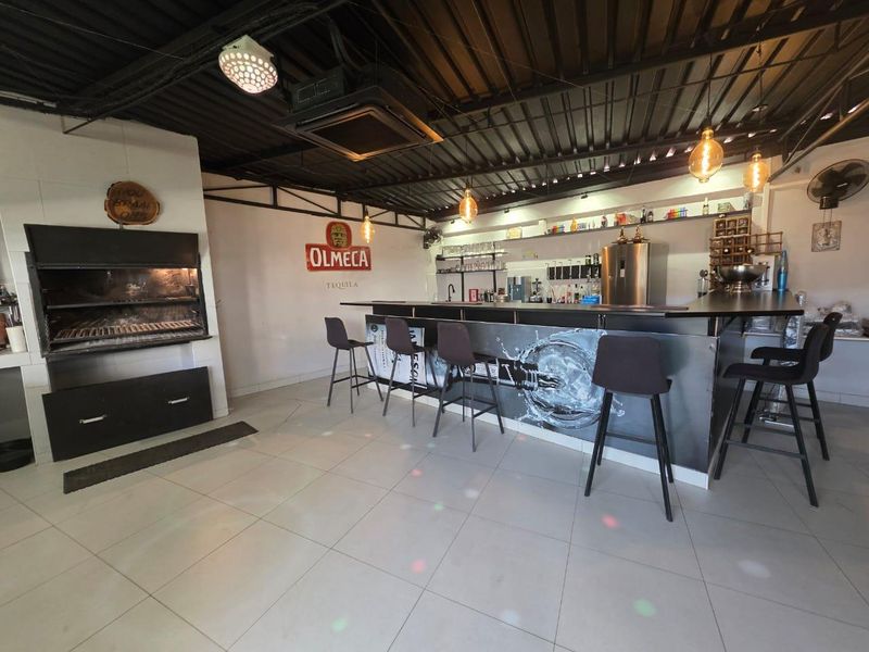 A dedicated entertainment bar area featuring a built-in braai, tiled flooring, and an industrial-style exposed ceiling with integrated bar counter.