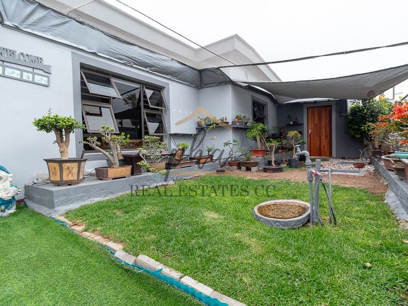 A rear courtyard area featuring a lawn, shade sail covering, and direct access to the home via a timber door and aluminium windows.