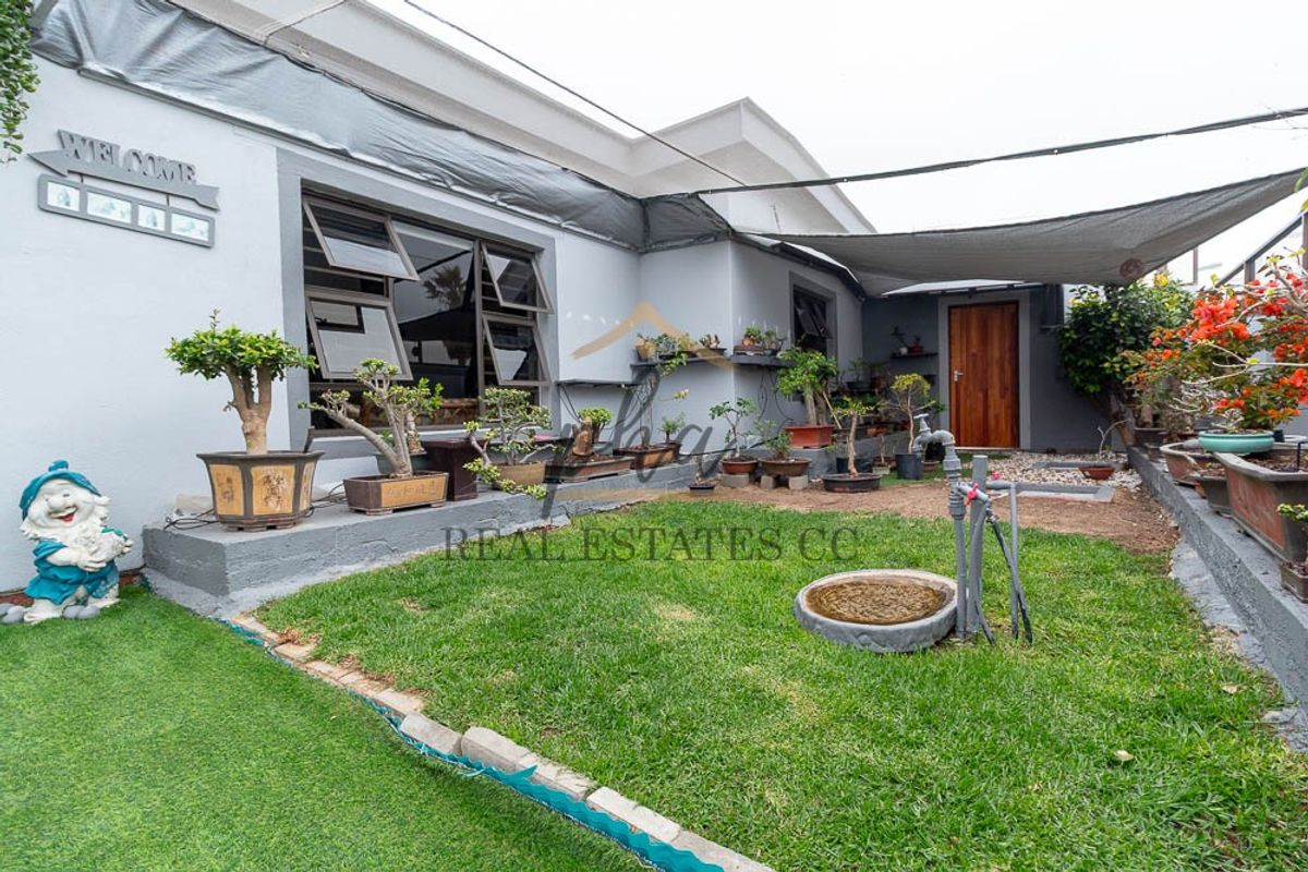 A rear courtyard area featuring a lawn, shade sail covering, and direct access to the home via a timber door and aluminium windows.