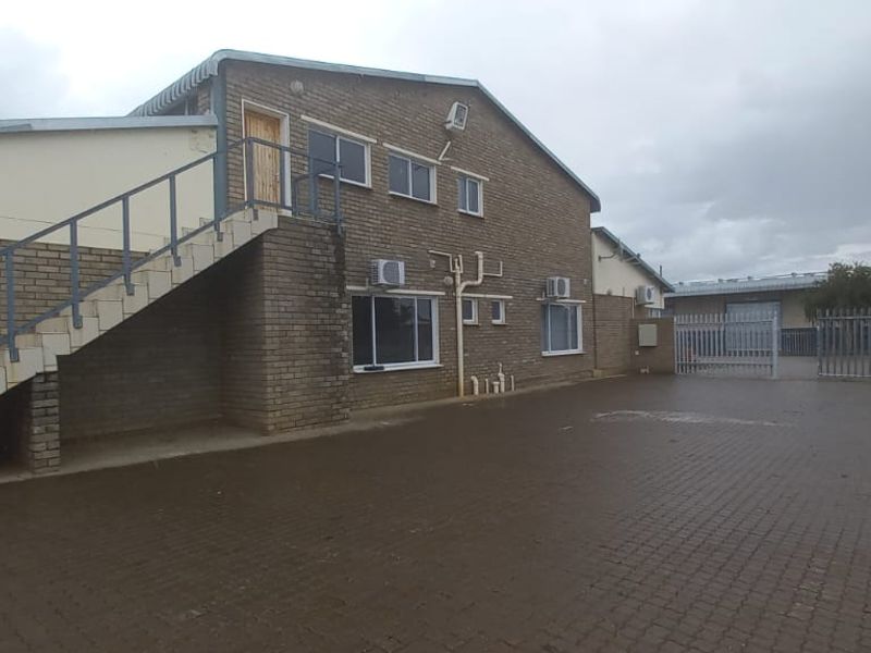 Rear view of an industrial property featuring a brick facade, external staircase, paved yard area, and secure gated access.