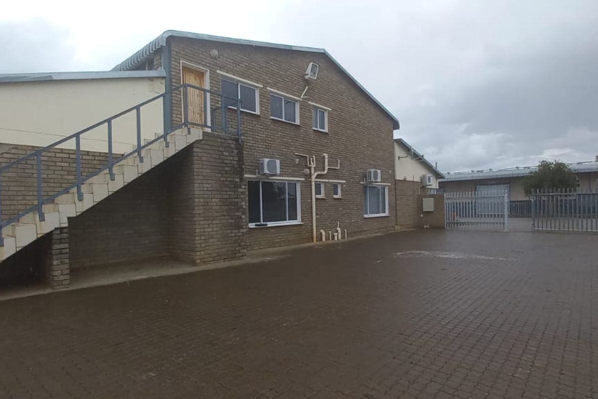 Rear view of an industrial property featuring a brick facade, external staircase, paved yard area, and secure gated access.