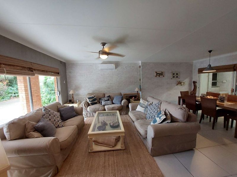 Spacious open-plan living and dining area featuring an exposed brick wall, split-system air conditioning, ceiling fan, and large sliding doors leading to the patio.