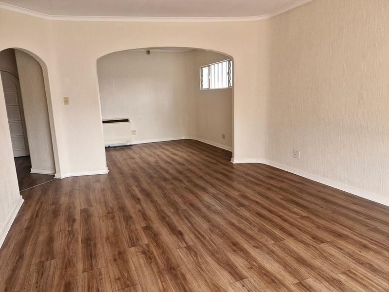 An empty living room featuring modern laminate flooring, an arched entryway, and a built-in electric wall heater.