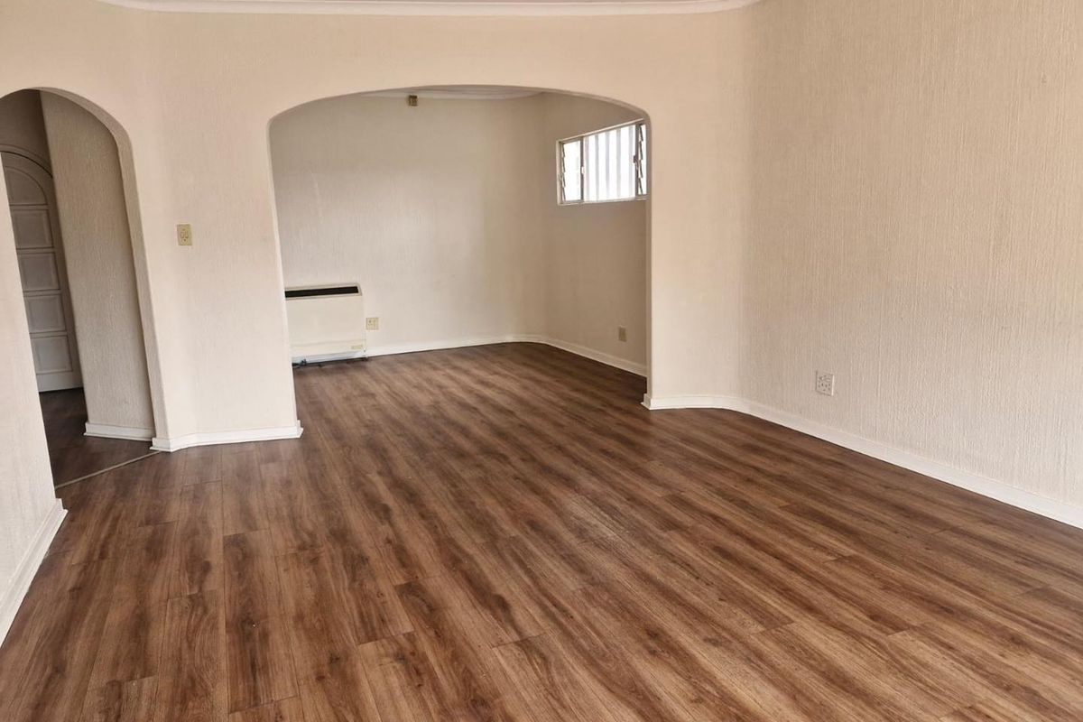 An empty living room featuring modern laminate flooring, an arched entryway, and a built-in electric wall heater.