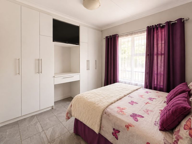 A well-maintained bedroom featuring extensive built-in white cabinetry, tiled flooring, and natural light through a window with purple curtains.