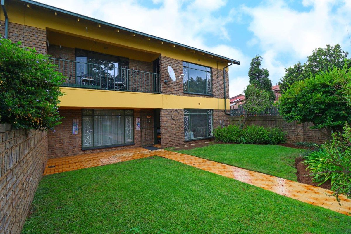 Rear view of a two-story brick apartment building featuring a private balcony, paved garden walkway, and well-maintained lawn area.