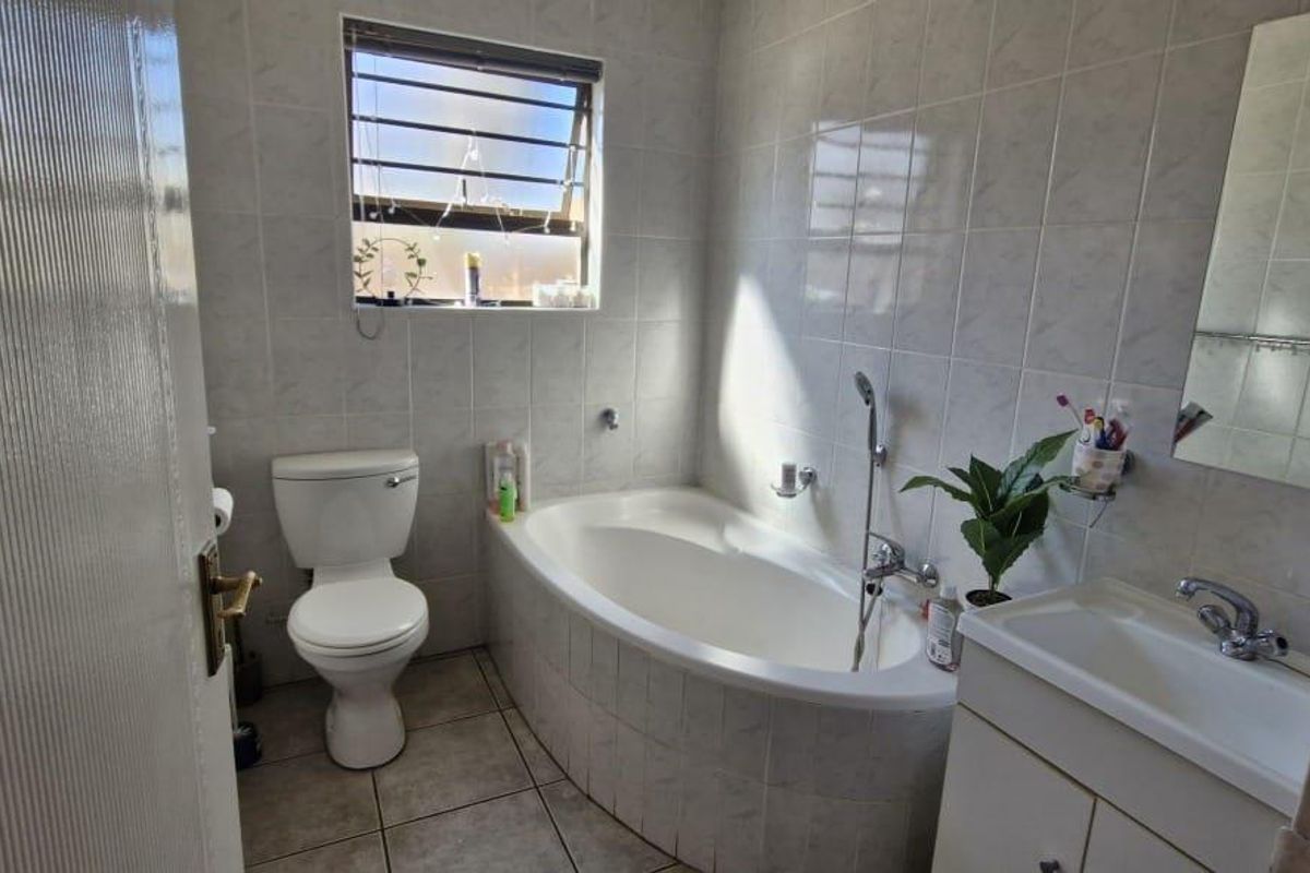 A functional bathroom featuring a built-in bathtub, a pedestal vanity with basin, and a toilet, finished with full-height wall tiling.
