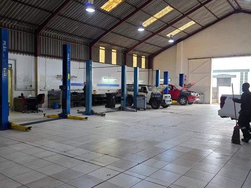 Spacious industrial workshop featuring multiple vehicle lifts, tiled flooring, high-clearance corrugated roofing with skylights, and large access doors for vehicle entry.
