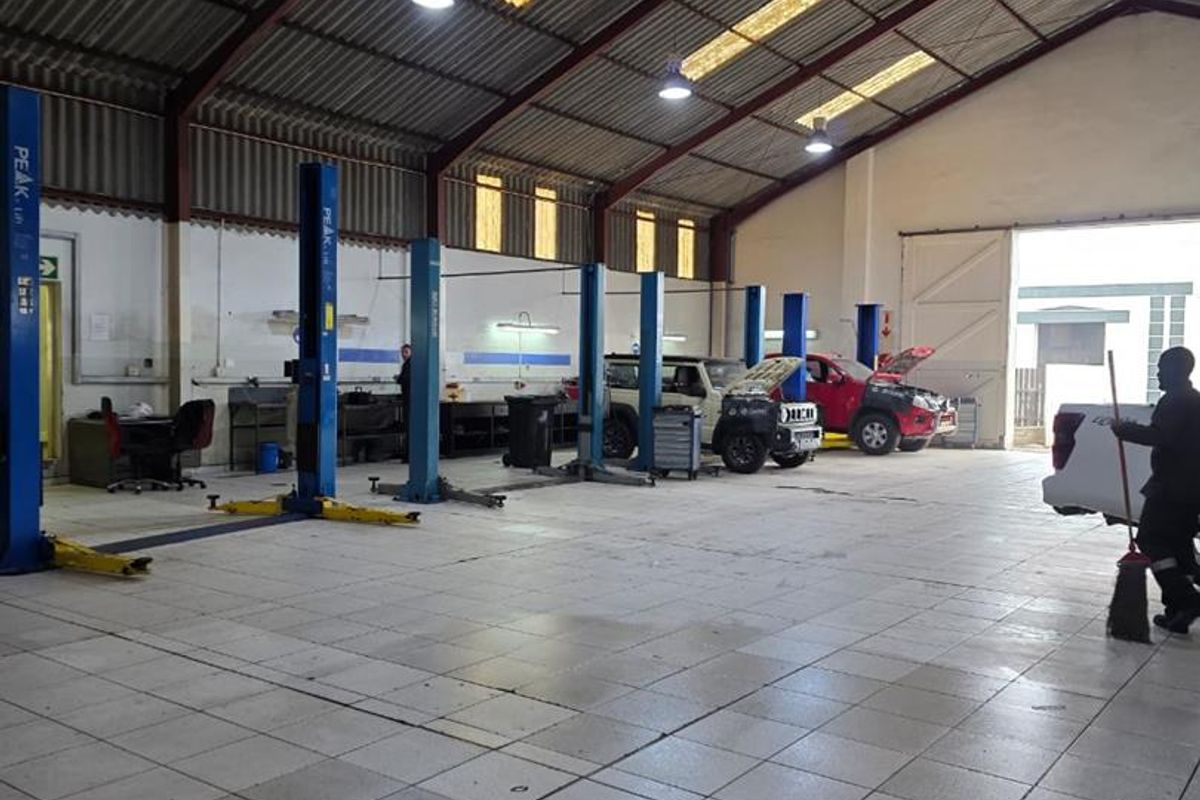 Spacious industrial workshop featuring multiple vehicle lifts, tiled flooring, high-clearance corrugated roofing with skylights, and large access doors for vehicle entry.
