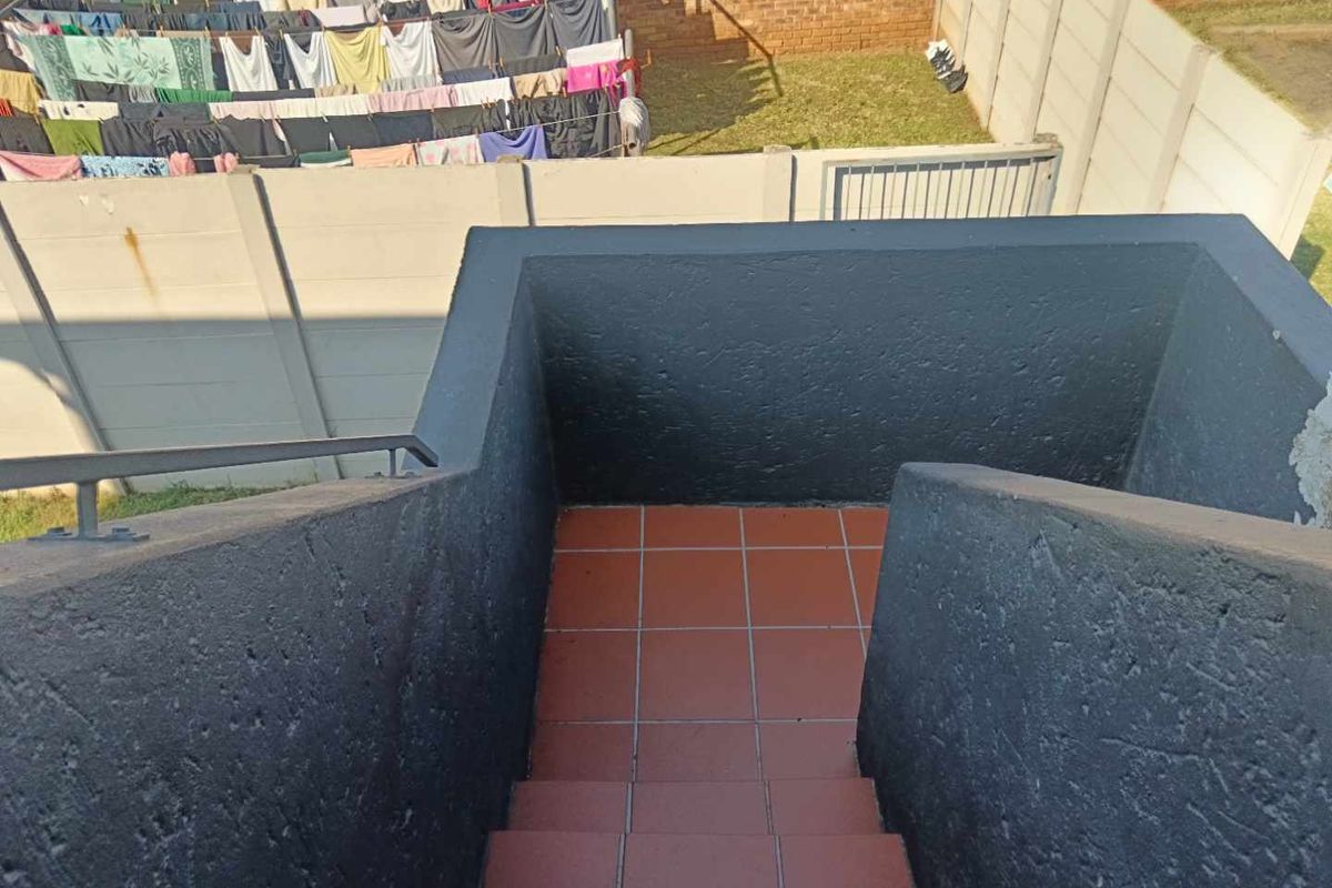 An exterior view of a tiled staircase leading down to a rear garden area enclosed by precast concrete boundary walls.