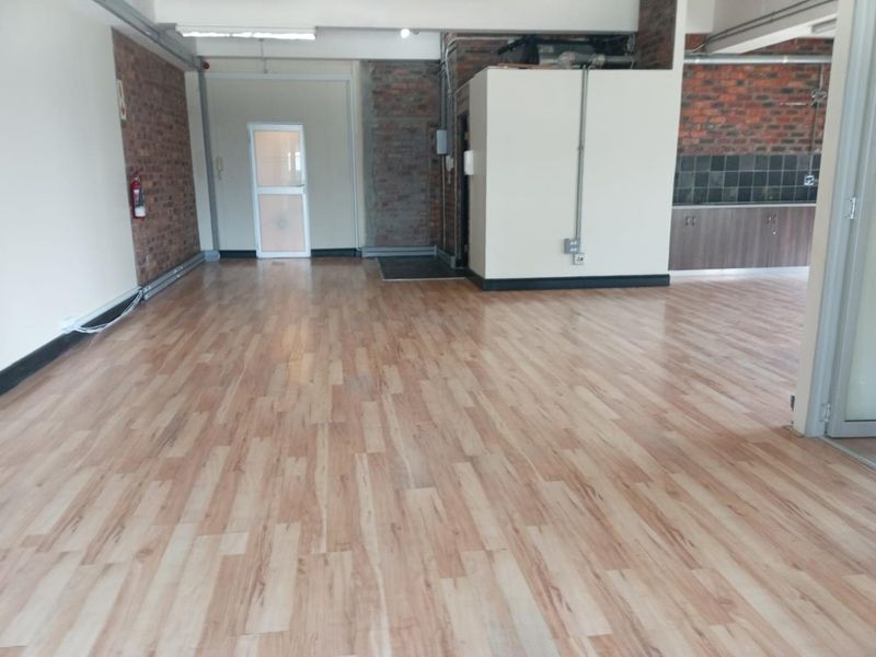 Spacious open-plan office area featuring exposed brick walls, laminate flooring, and a small kitchenette corner with built-in cabinetry.