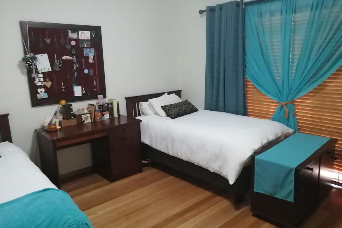 A well-maintained bedroom featuring timber flooring, window blinds, and a wall-mounted air conditioning unit.